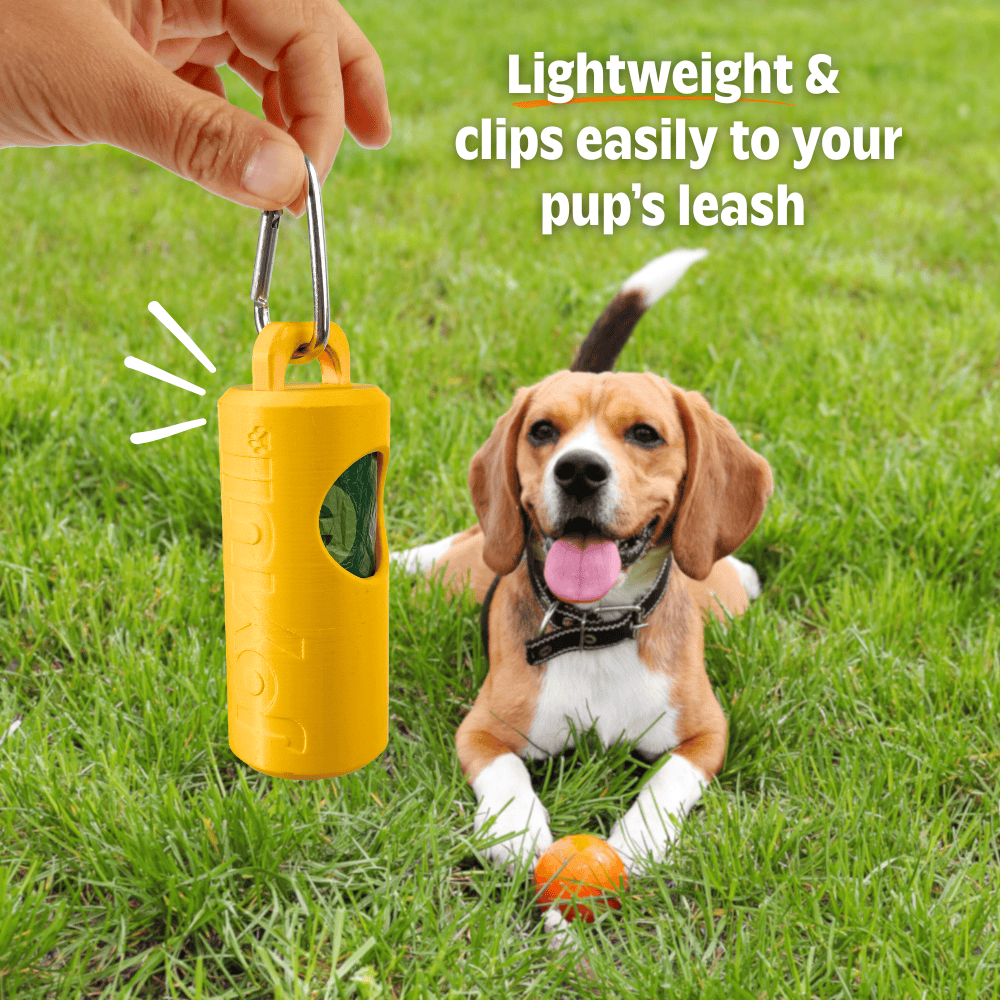 Yellow dog training clicker with a clip, held by a hand, on grass with a dog in the background.